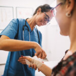 Professional nurse at the hospital bandaging the hand with a medical bandage for a woman patient.